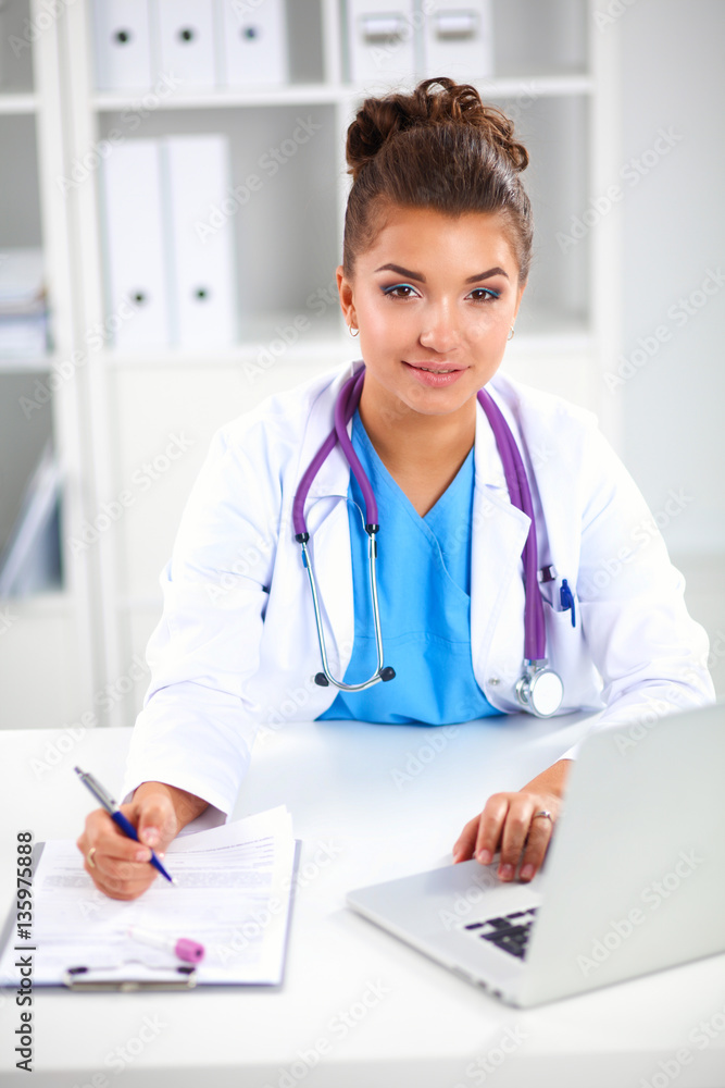 Beautiful young smiling female doctor sitting at the desk and writing. Beautiful young smiling female doctor sitting at the desk and writing.