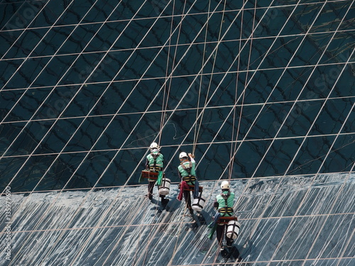 men cleaning glass building by rope access at height