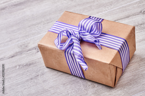 Gift box on wooden backdrop. Striped ribbon bow on present.