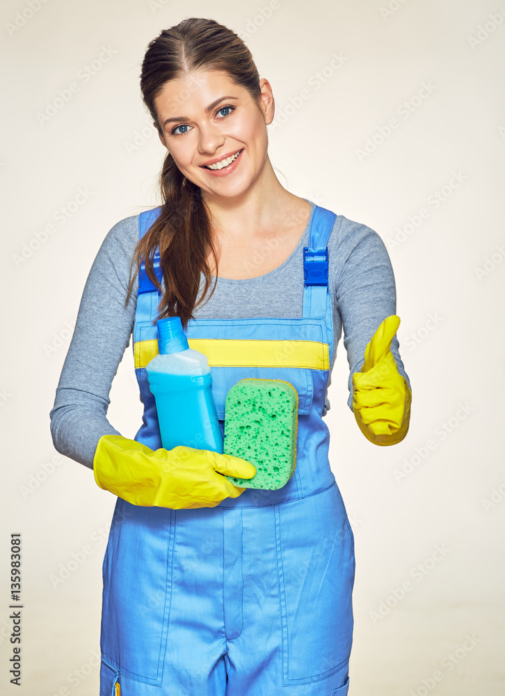 Woman wearing coveralls show thumb up holding sleanser with spo Woman wearing coveralls show thumb up holding sleanser with spo