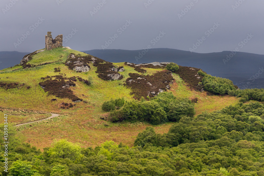 North Coast, Scotland - June 6, 2012: On a bright green hilltop stand the remains of a castle tower near the village of Tongue under a dark gray sky. Foreground, hill with many hues of green. North Coast, Scotland - June 6, 2012: On a bright green hilltop stand the remains of a castle tower near the village of Tongue under a dark gray sky. Foreground, hill with many hues of green.