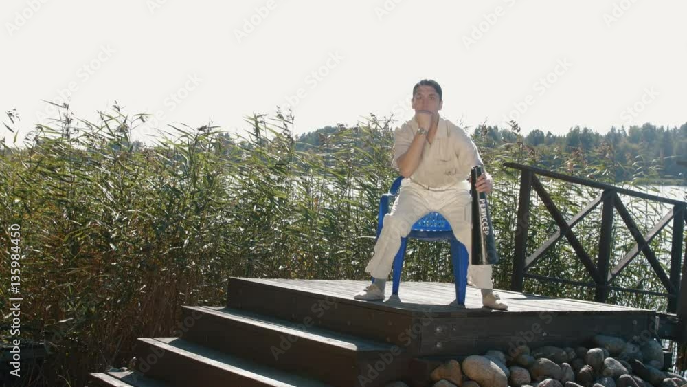 Movie director in hair net and white clothes absorbedly reacting on acting scene, sitting on wooden structure on lake shore on sunny summer day Movie director in hair net and white clothes absorbedly reacting on acting scene, sitting on wooden structure on lake shore on sunny summer day
