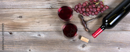 Unopen bottle of red wine and glasses with grapes on rustic wood