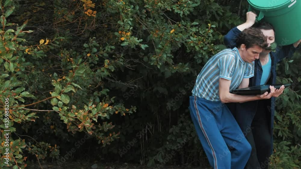 Two man coming out shaking shrub with trash can and monitor tablet on summer day Two man coming out shaking shrub with trash can and monitor tablet on summer day