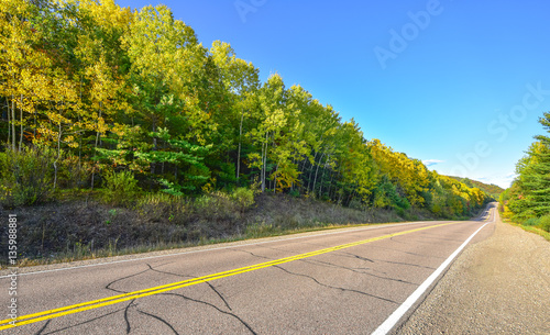 Summer highway open road to anywhere.
Sunny blue sky, woods on either side down a country highway in summer.  