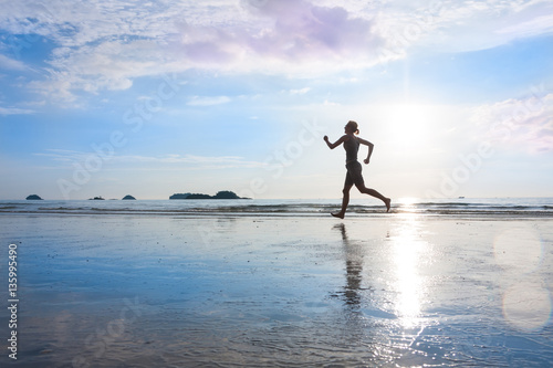 Silhouette of jogging woman at sunset or sunrise wet beach with beautiful reflection on sand. Healthy lifestyle, fitness concept.