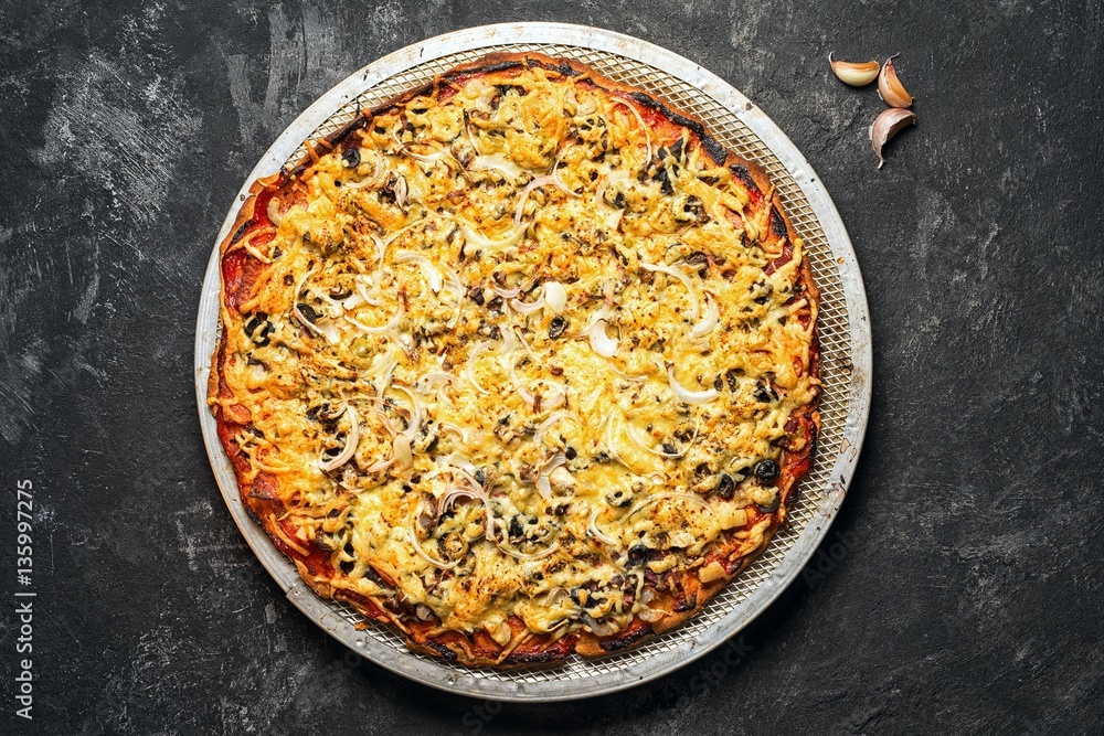 freshly cooked pizza on a circular grid in the oven, lying in the middle of the dark black cement background . freshly cooked pizza on a circular grid in the oven, lying in the middle of the dark black cement background .