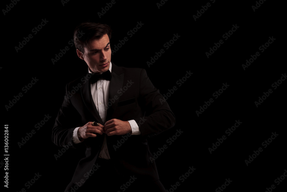 elegant man buttoning his tuxedo and looks to side elegant man buttoning his tuxedo and looks to side