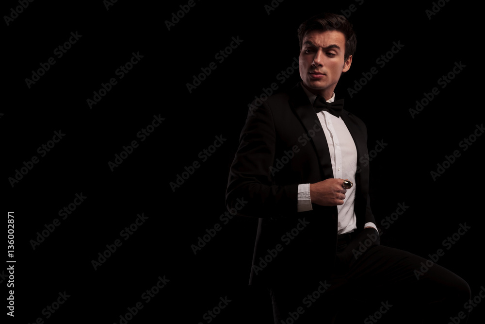 arrogant young man in tuxedo and bowtie looking back