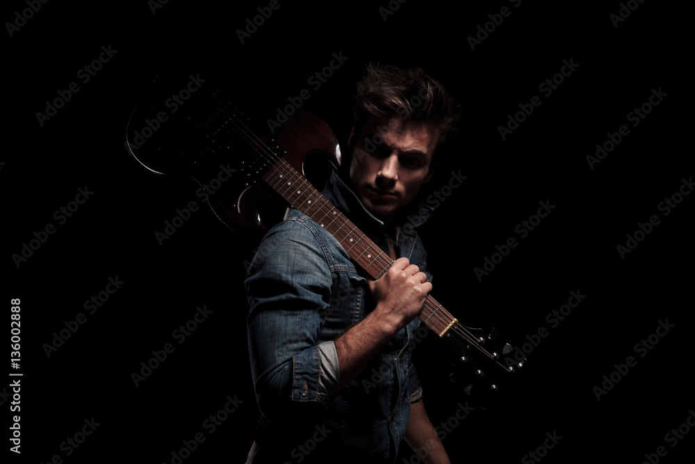 dramatic young guitarist looking back while holding guitar on sh dramatic young guitarist looking back while holding guitar on sh