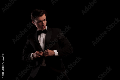 elegant man buttoning his tuxedo and looks to side