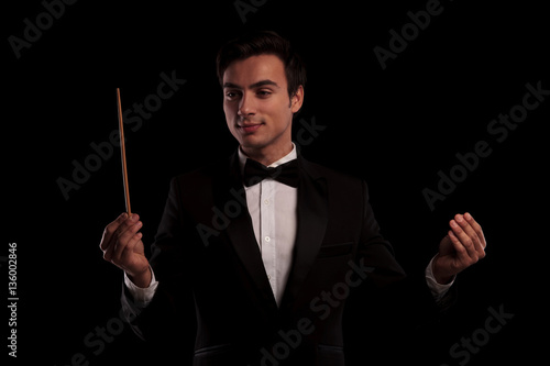 elegant man in tuxedo conducting an orchestra , business concept, on black studio background