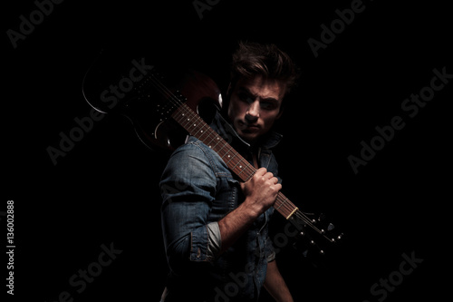 dramatic young guitarist looking back while holding guitar on sh