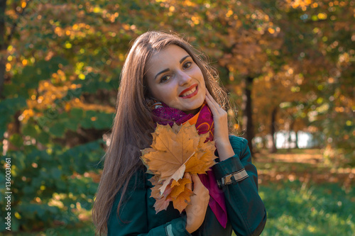cute girl with long hair in the Park keeps the Maple leaves in hands and smiles