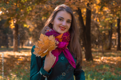 beautiful smiling girl with a pink scarf holding  bouquet of leaves