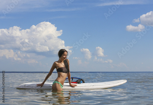 Young beautiful girl is standing near the surf desk in the sea
