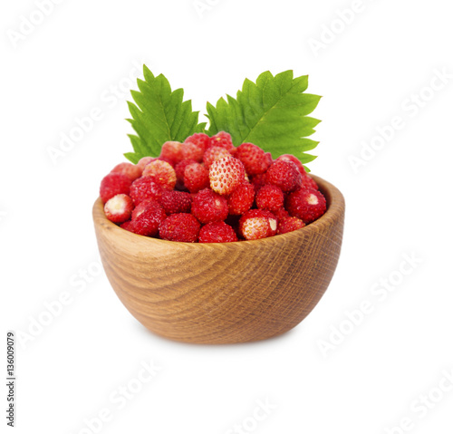 Wild small strawberries in a wooden bowl with leaves. Ripe and tasty strawberries isolated on white background. Sweet and juicy berry with copy space for text.