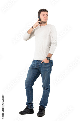 Upset man talking on the phone looking back over the shoulder. Full body length portrait isolated over white studio background. 