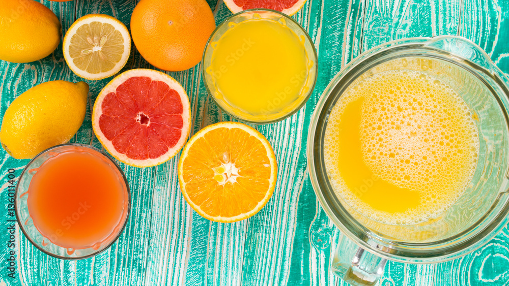 fresh juice from citrus fruits - lemon, grapefruit, orange, pine apple in blender bowl and glasses on turquoise colored wooden background, top view fresh juice from citrus fruits - lemon, grapefruit, orange, pine apple in blender bowl and glasses on turquoise colored wooden background, top view