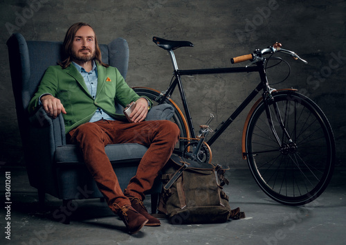 A man sits on a chair with bicycle on background.
