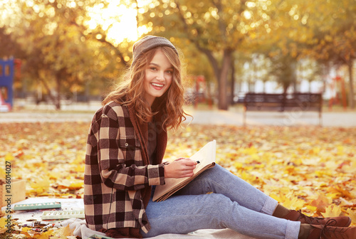 Young female artist drawing sketch while sitting on ground in autumn park