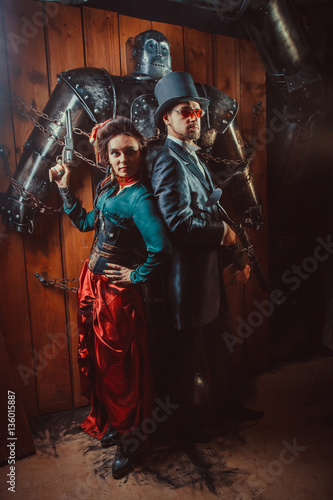 Beautiful couple with the guns and big tied robot on the background.