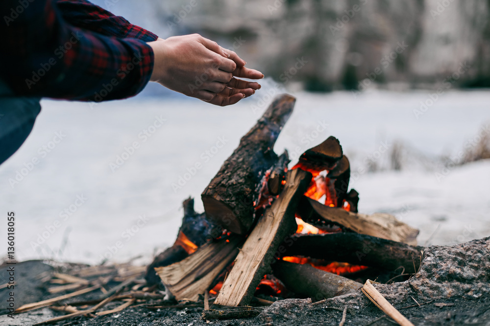 Obraz premium Girl warms hands near a fire in winter. Rocks on background
