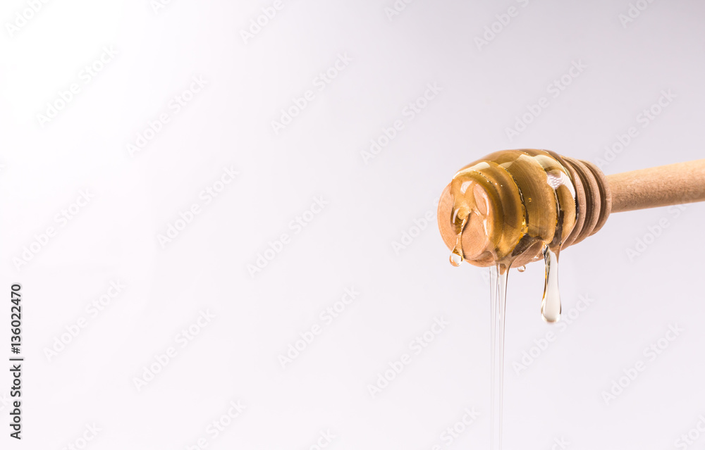 Honey dripping from a wooden honey dipper isolated on white