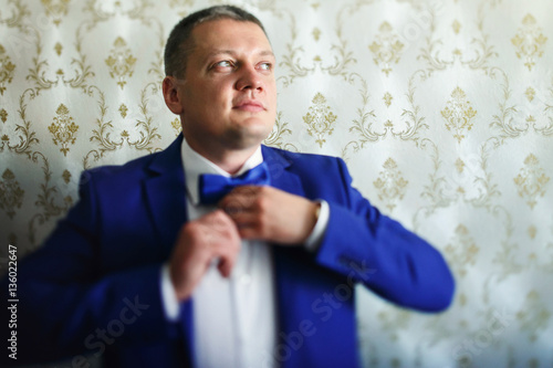 Groom in blue suit fixes blue bow tie on his neck