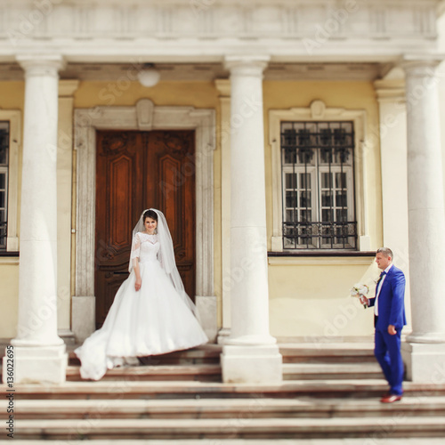 Groom in blue suit looks at bride while she stands before old wo