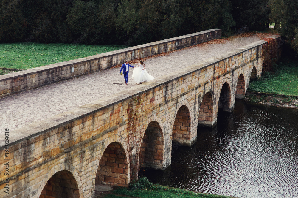 Look from above at newlyweds running along the bridge over the r Look from above at newlyweds running along the bridge over the r