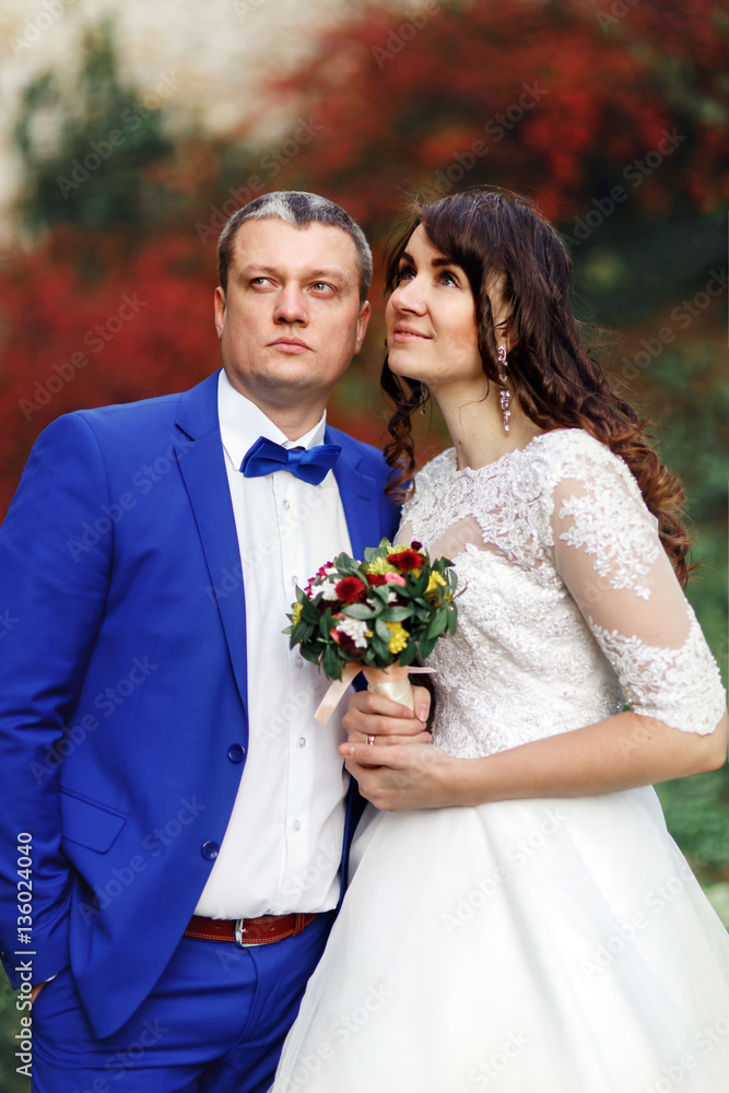 Bride and groom look up in the sky posing before red autumn bush Bride and groom look up in the sky posing before red autumn bush