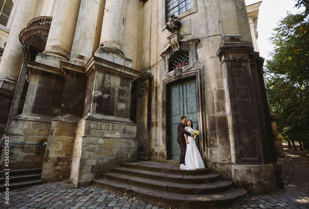 Groom embraces his bride next to the entrance to the church