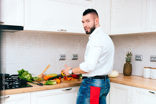 Handsome elegant man cooking and preparing lunch. Young cook smiling and making a salad