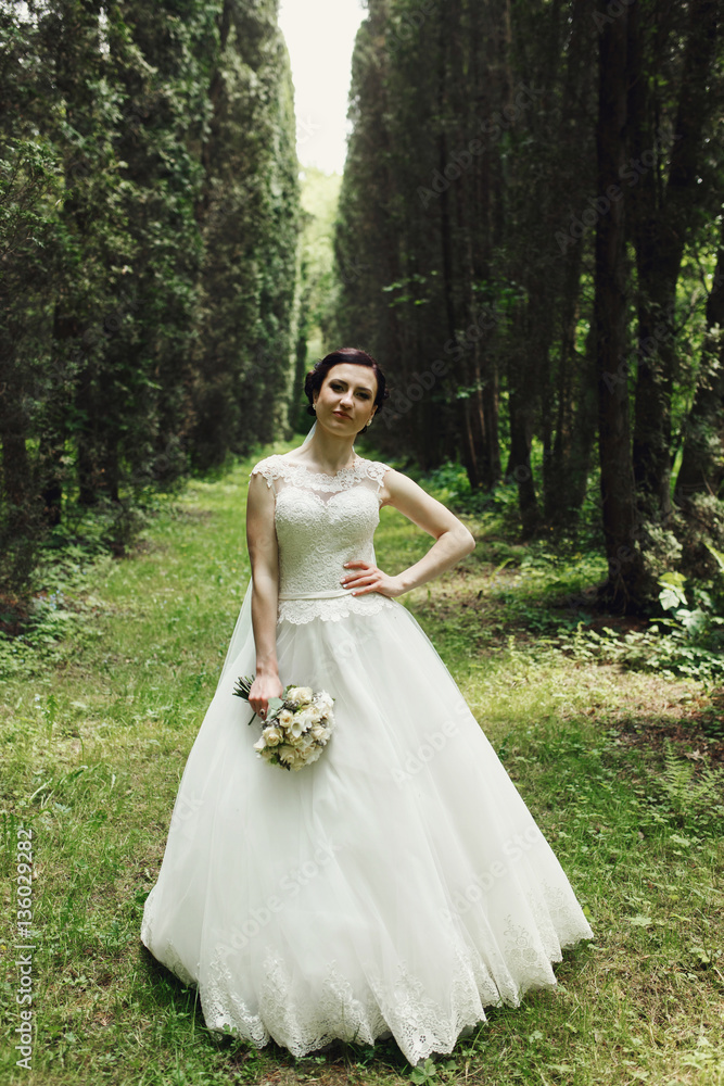 Bride holds her hand with bouquet down while she poses in green Bride holds her hand with bouquet down while she poses in green