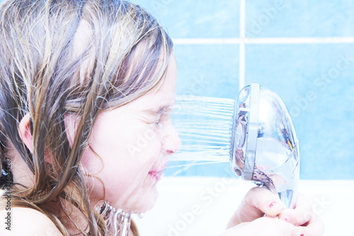 Child girl pours water from the shower at her face in bathtub