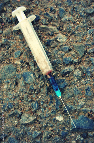 Syringe lying on the earth surface with spot of blood