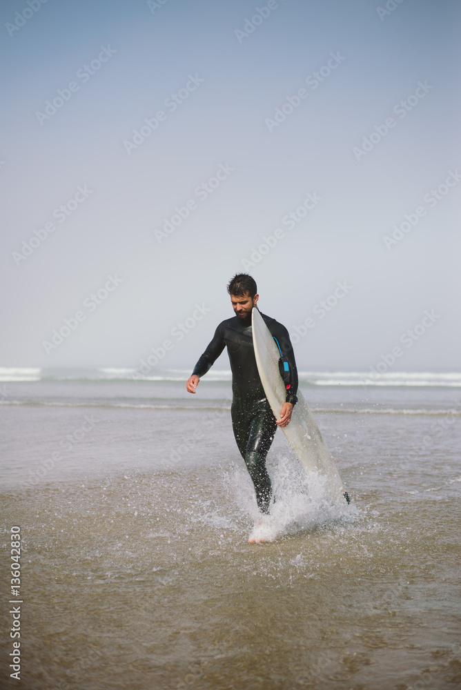 Surfer in wetsuit with his surfboard leaving the sea after surfing