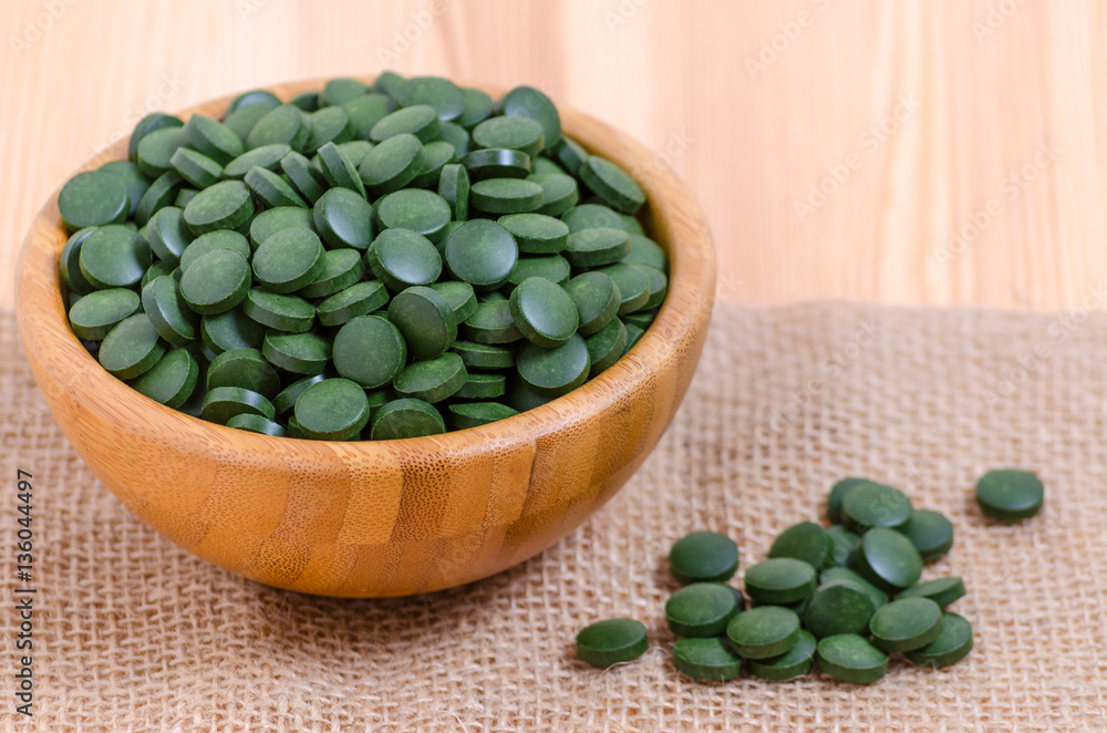 green pills spirulina and chlorella seaweed close up in a wooden bowl green pills spirulina and chlorella seaweed close up in a wooden bowl