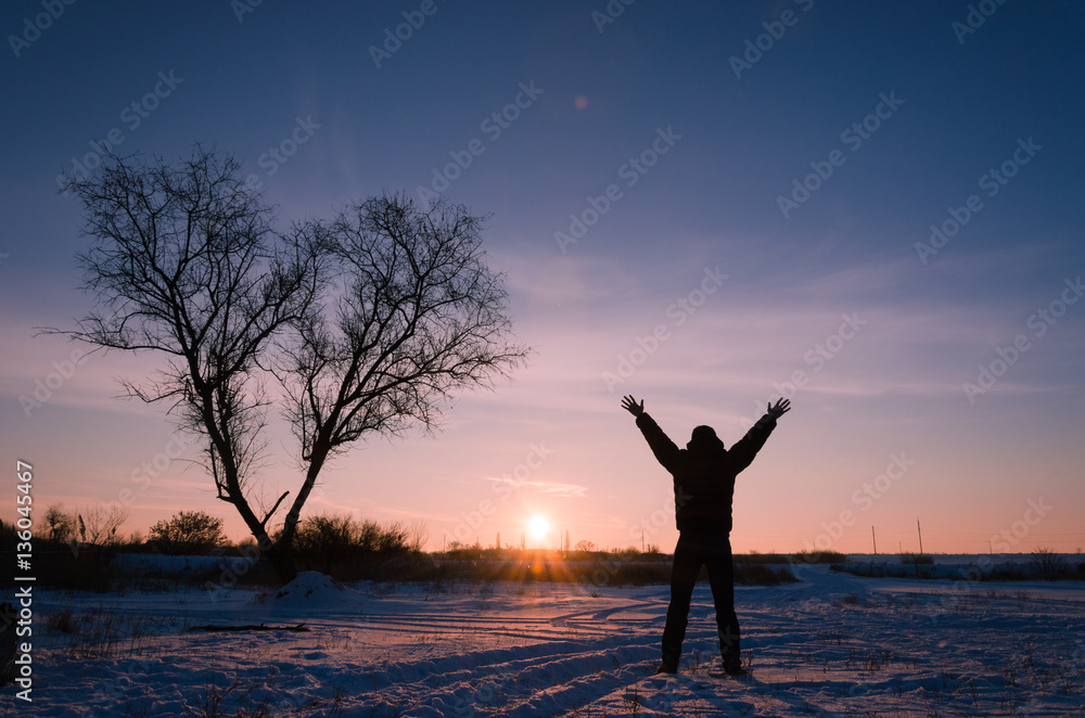 Tree in snow scene with dramatic sunset and jumping man hands up