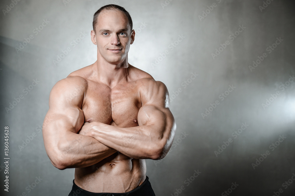 Brutal strong bodybuilder man posing in studio on grey backgroun