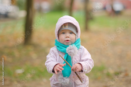 little girl in a pink jacket and turquoise scarf autumn in the park with a cane in his hand