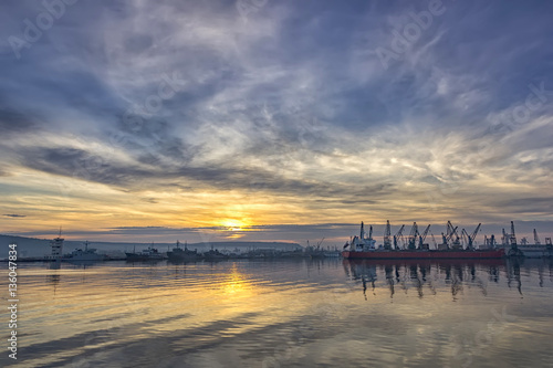 Landscape of ship and cranes in port at sunset.