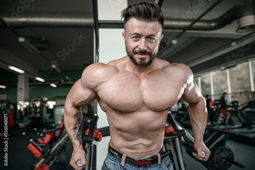 Brutal strong bodybuilder man pumping up muscles and train gym