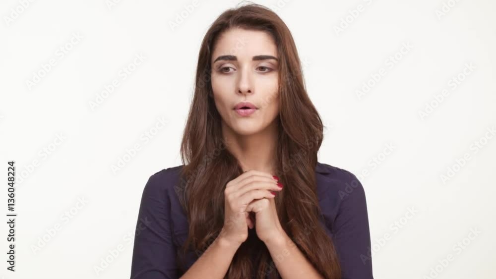 Nervous beautiful Caucasian female with long brown hair wearing dark blue shirt standing kicking her heels rubing hands biting nails on white background in slowmotion Nervous beautiful Caucasian female with long brown hair wearing dark blue shirt standing kicking her heels rubing hands biting nails on white background in slowmotion