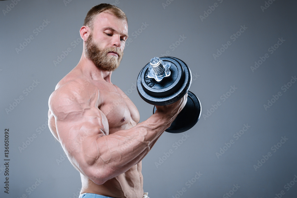 Brutal strong bodybuilder man posing in studio on grey backgroun Brutal strong bodybuilder man posing in studio on grey backgroun