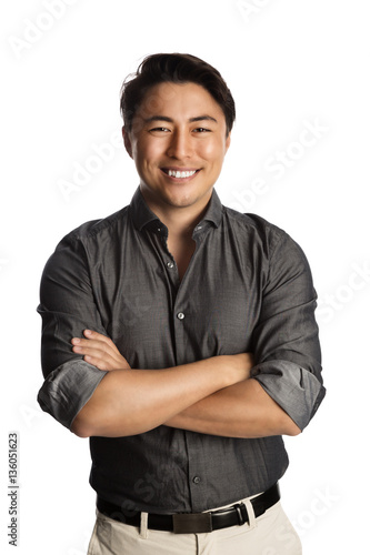 Slika na platnu Cool laid back man wearing a grey shirt with rolled up sleeves and khaki pants, standing with a big smile against a white background
