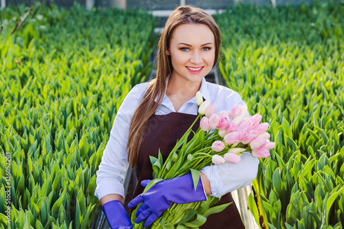 Schilderij op canvas Woman gardener florist holding a bouquet of flowers, standing in a greenhouse, w