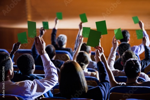 Rear view of business executives show their approval by raising hands at conference center photo
