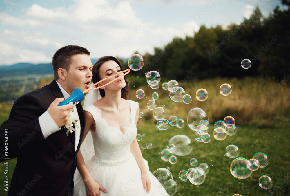 beautiful and young bride and groom inflating bubbles outdoors